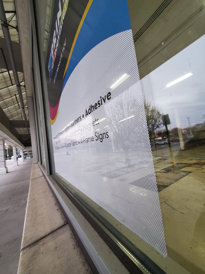Custom perforated window film with Print With Provision branding, viewed from outside at an angle, installed on storefront window for promotional advertising.