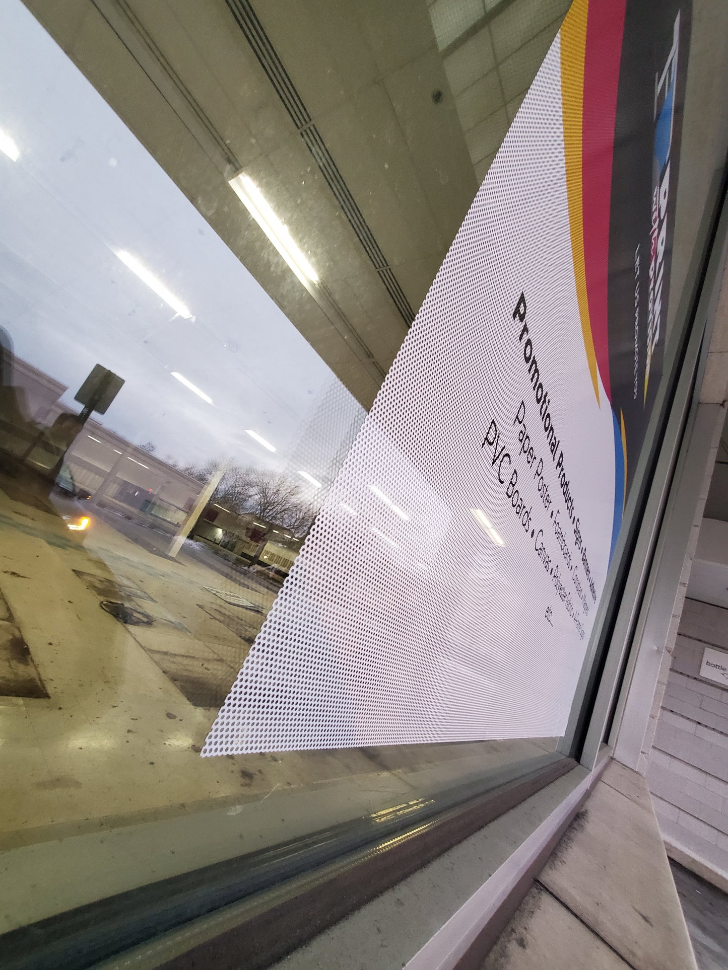 Print With Provision custom perforated window film installed on storefront glass, exterior side angle view showing see-through vinyl for promotional advertising.