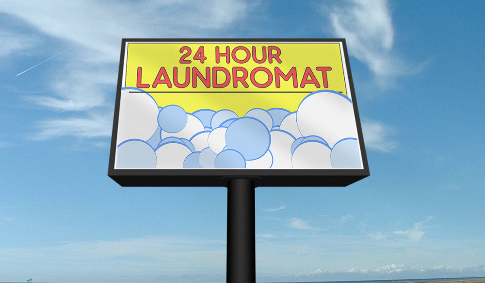24 hour laundromat backlit banner sign with bubbles graphic, displayed outdoors on a billboard during daytime.